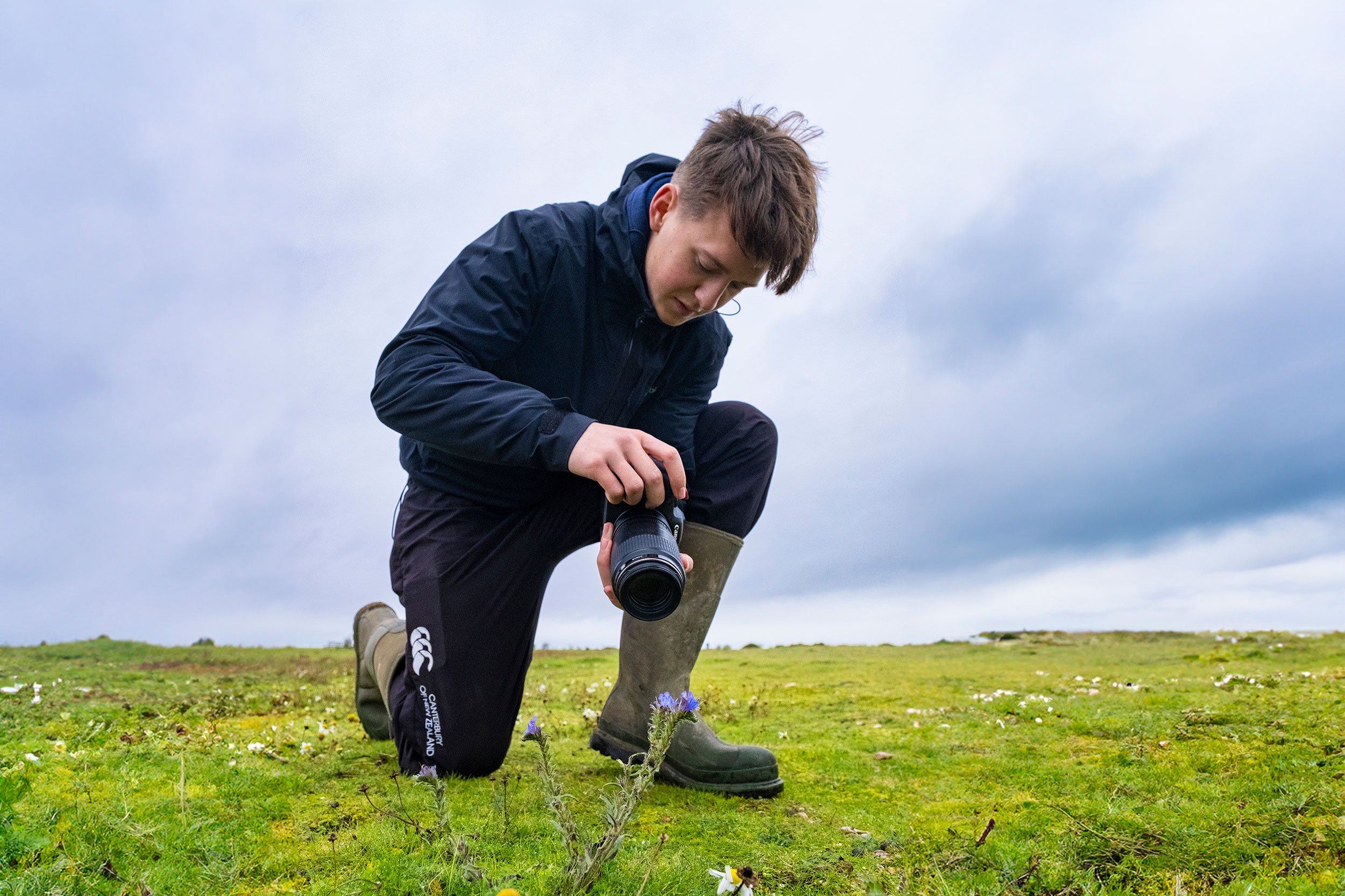 A young person is taking a close-up photo of a flower in a field