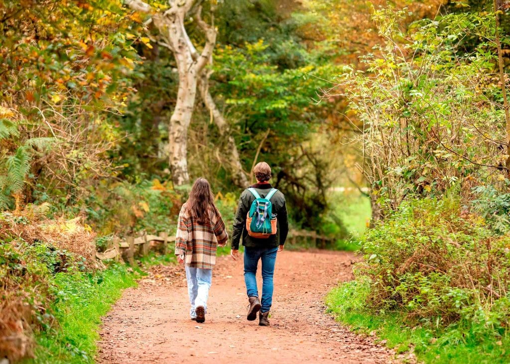 A man and woman walk through an autumnal woodland path