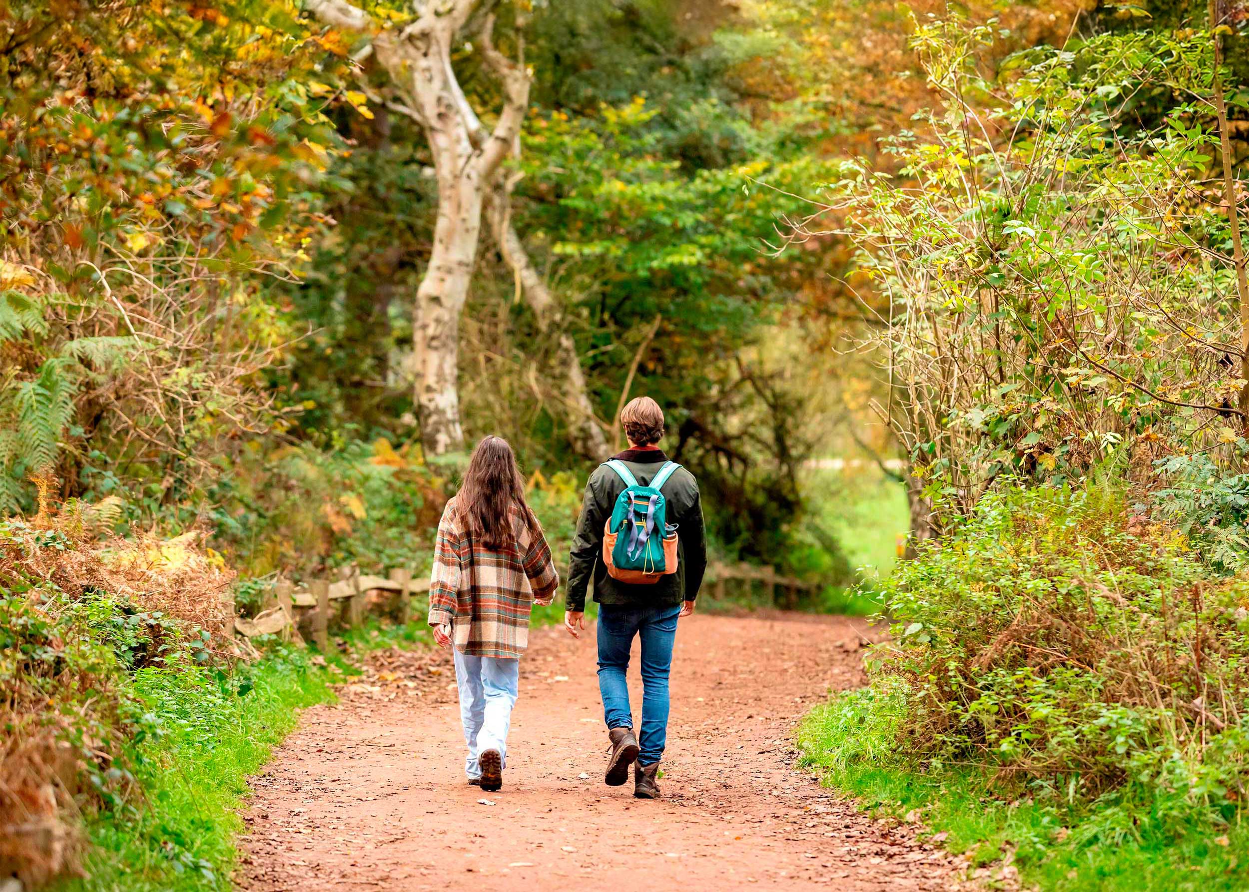 A man and woman walk through an autumnal woodland path