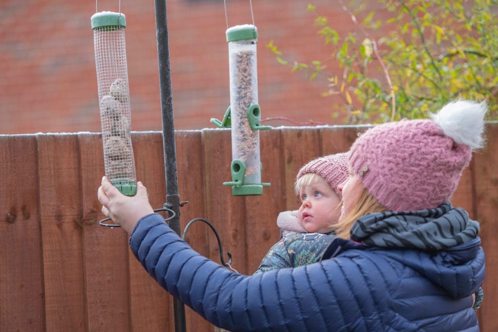 A young daughter and mother topping up bird feeders in a garden