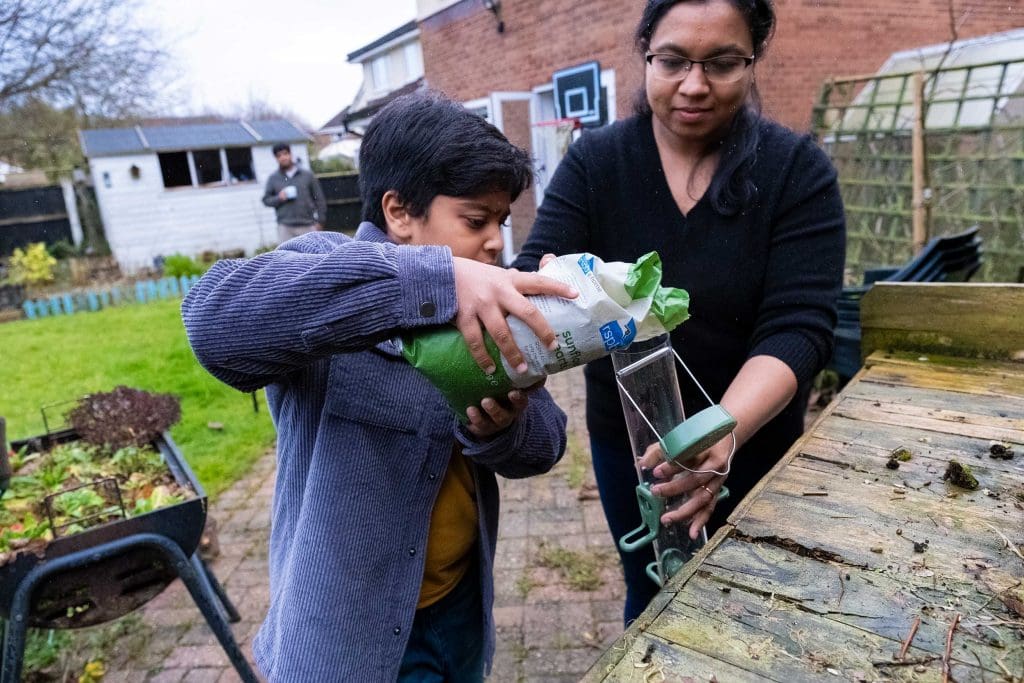 A young boy and a woman pour sunflower eats into a bird feeder